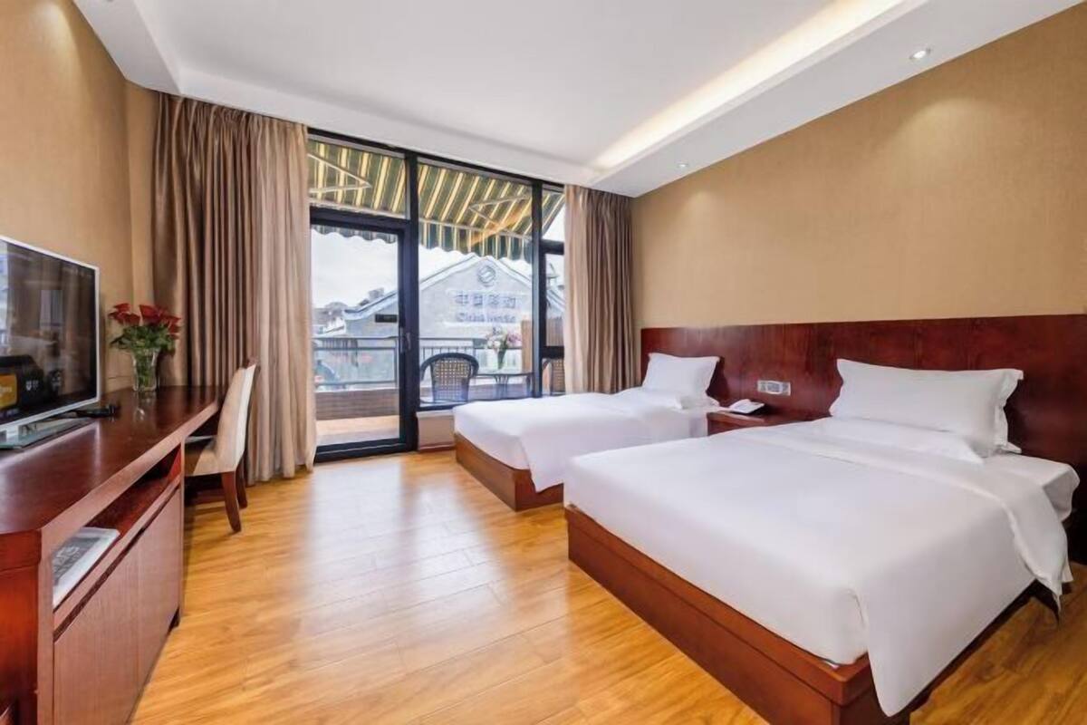 Une chambre d’hôtel avec deux lits, une télévision, un bureau et un balcon donnant sur des immeubles.