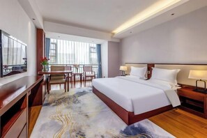 A hotel room with a large bed, a desk with a chair, a TV, and a view of the outside through large windows. - Li Jing Hotel Mile (Mile)