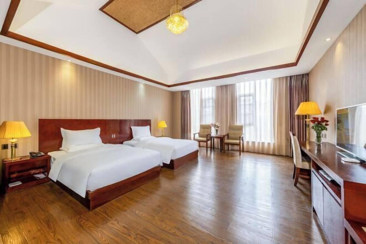 Une chambre d’hôtel avec deux lits, un bureau, une chaise, une télévision et une lampe.