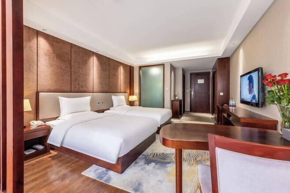 Une chambre d’hôtel avec deux lits, un bureau, une chaise, une télévision et une salle de bain visible à travers une porte ouverte.