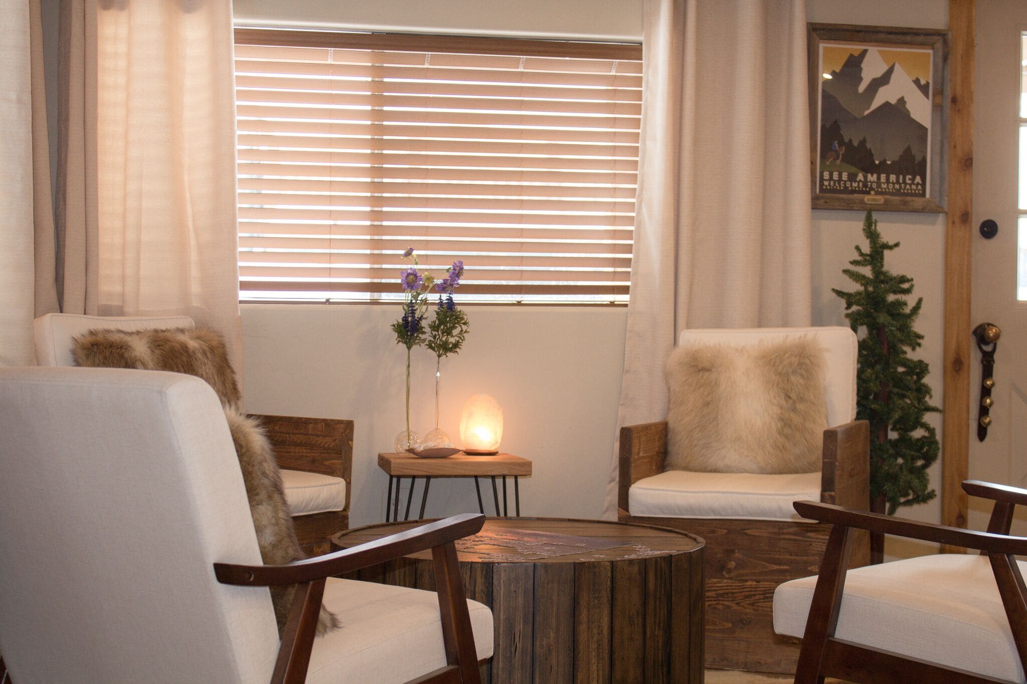 Ein gemütliches Wohnzimmer mit zwei weißen Sesseln, einem Holztisch und einem kleinen Beistelltisch mit Blumen in einer Vase und einer Lampe.