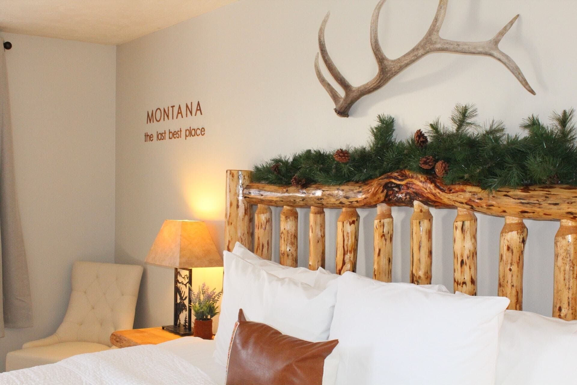 A bedroom with a bed, a lamp, a wall-mounted deer antler, and a sign reading "MONTANA the last best place".
