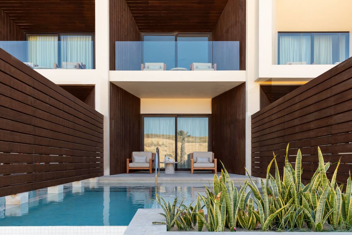 A modern hotel with a pool, two lounge chairs, and a view of the desert.