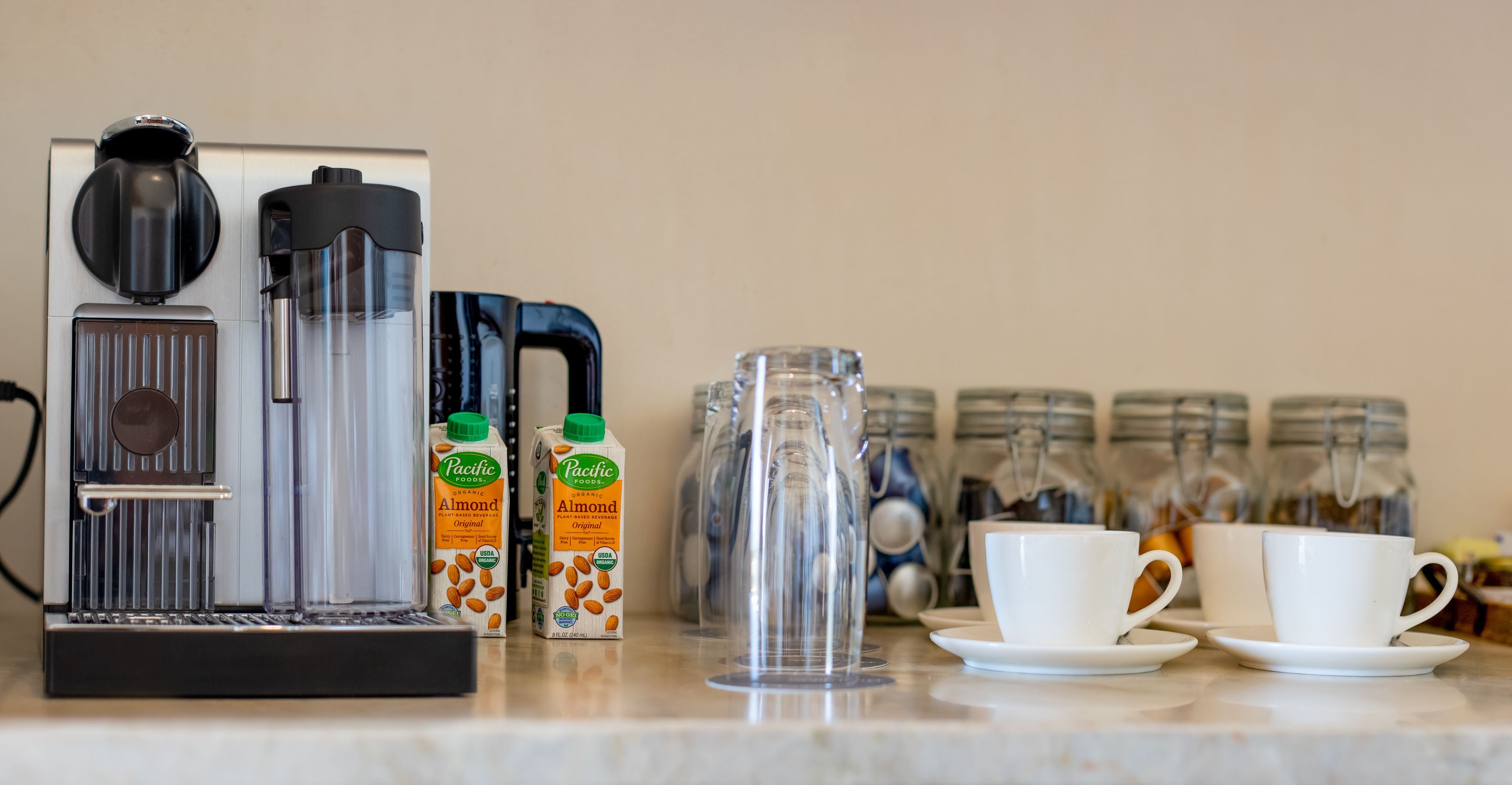 Eine Kaffeestation mit Kaffeemaschine, Mandelmilchkartons, einem Krug und Tassen.