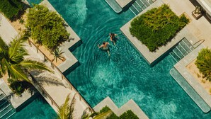 Une vue aérienne d’une piscine à l’eau d’un bleu limpide, entourée d’une végétation luxuriante et bordée d’une architecture moderne.
