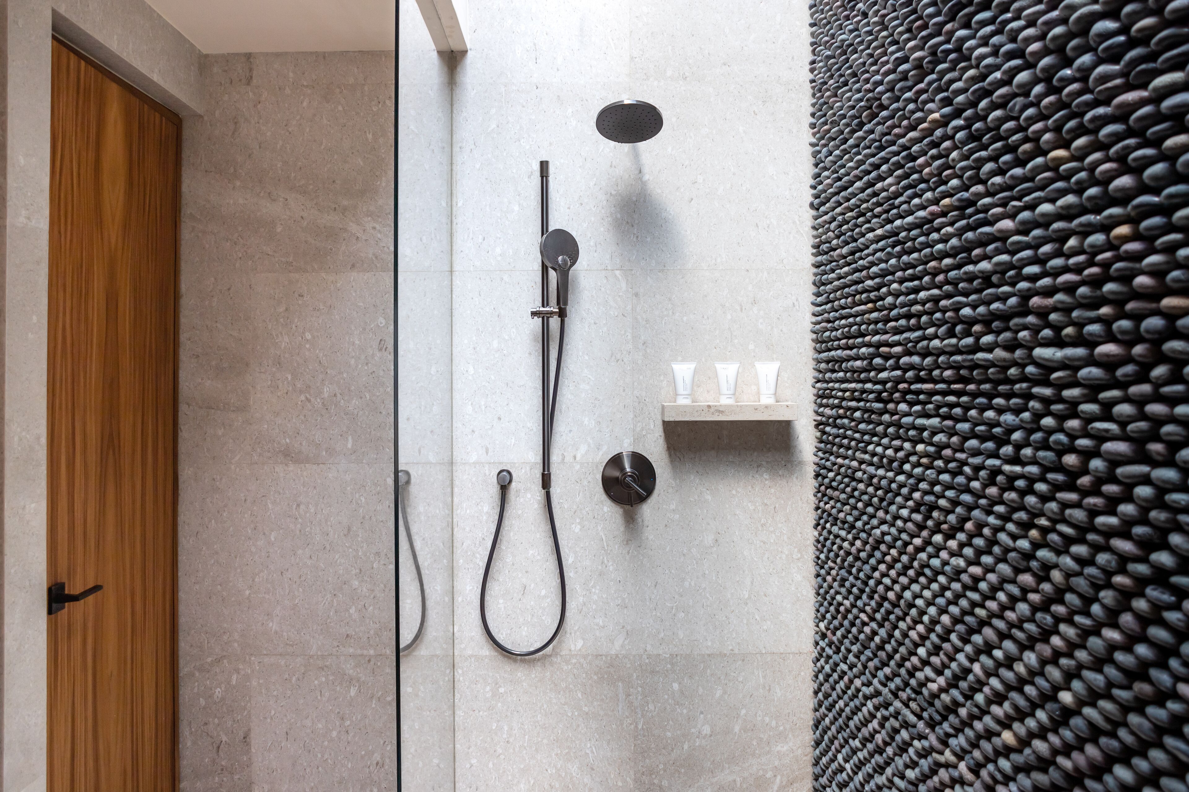 A modern shower area with a rain showerhead, handheld showerhead, and a wall-mounted control panel.