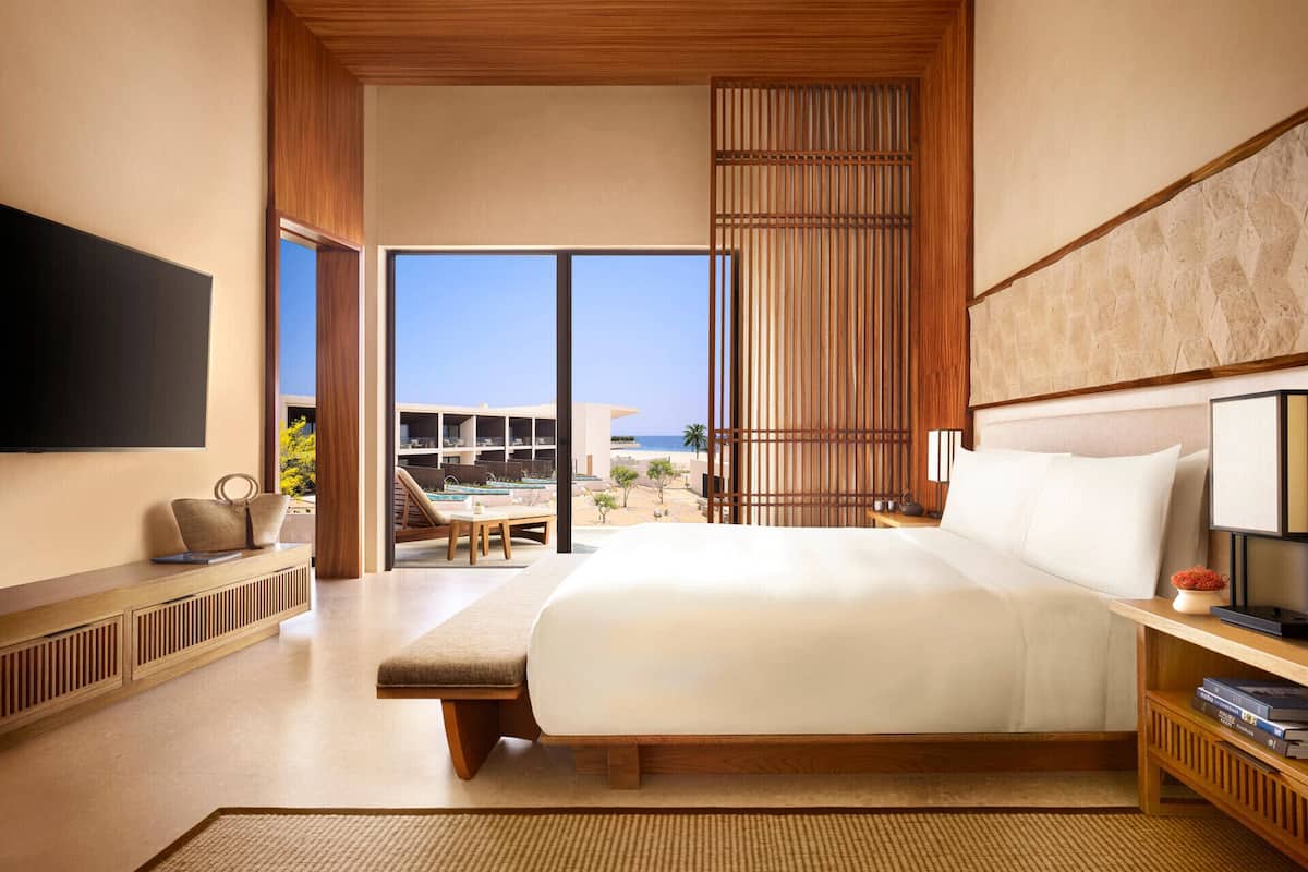 A modern hotel room with a large bed, a TV, a seating area with a view of the beach, and a balcony.