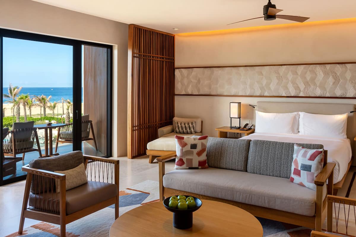 A hotel room with a bed, a sofa, a dining table, and a view of the ocean.