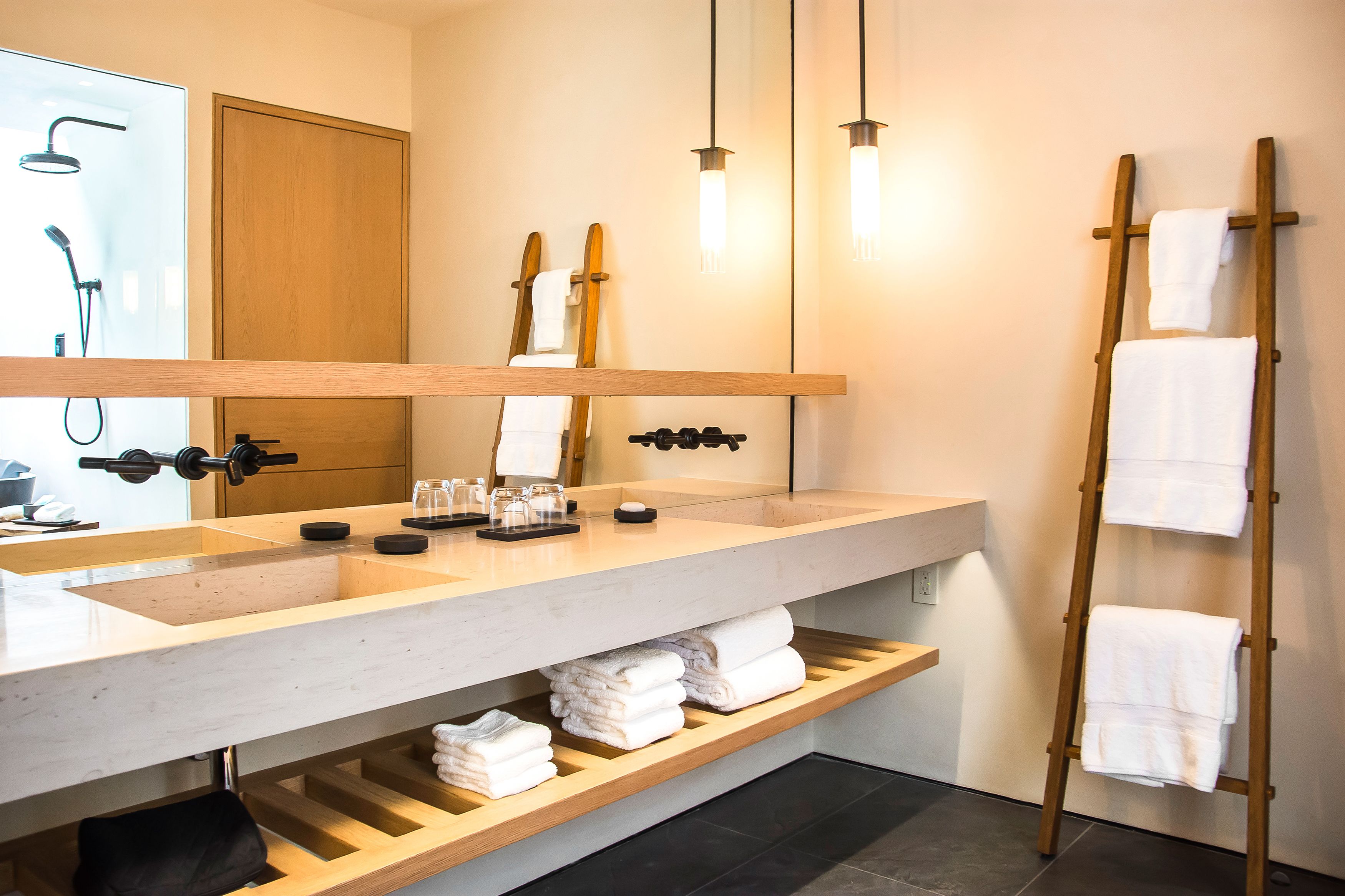 A modern bathroom with a large mirror, dual sinks, and a wooden towel rack.