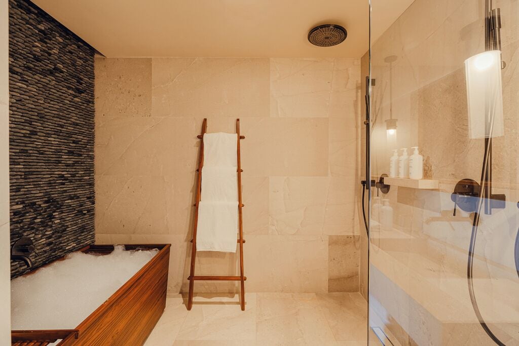 Een badkamer met een houten bad, een glazen douchecabine en een stenen muur.