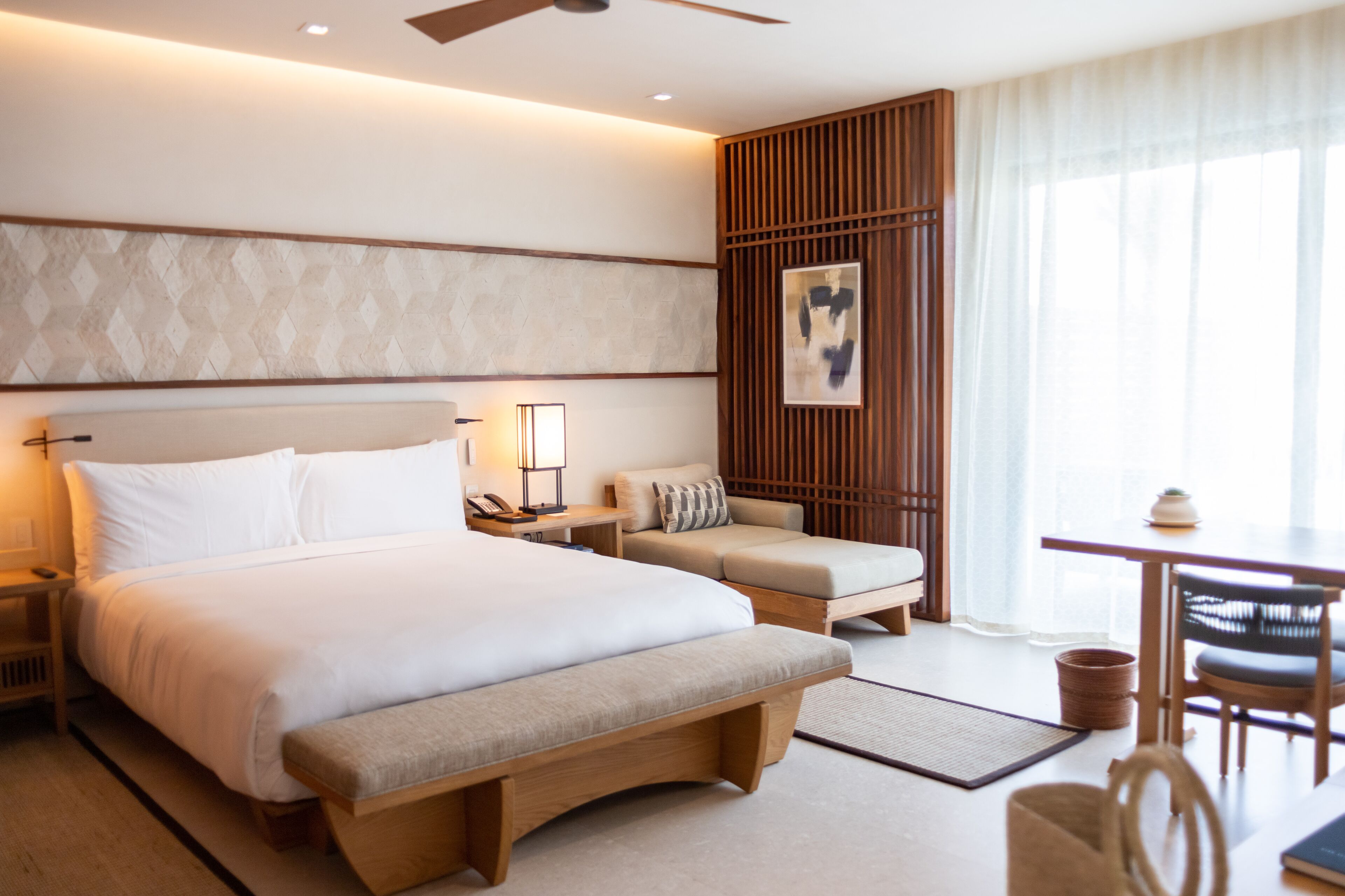 Habitación de hotel con una cama grande, un escritorio, una silla, un banco y vistas al exterior.