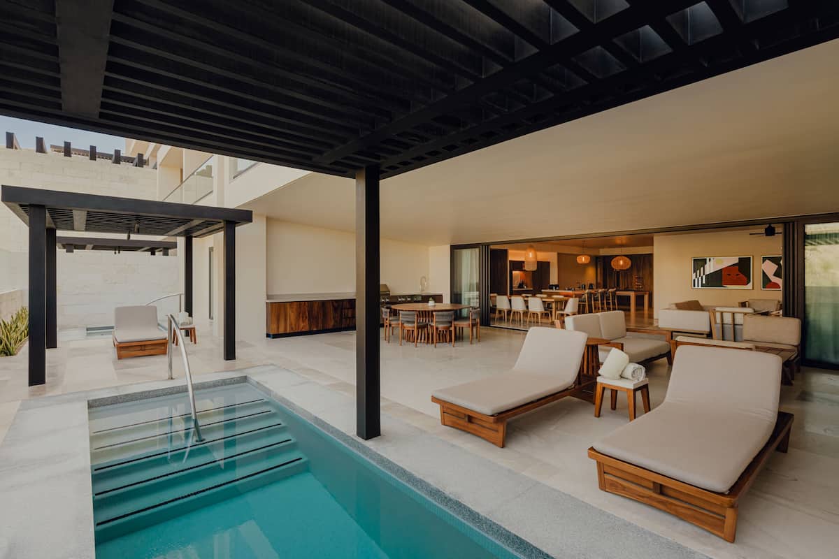 A modern outdoor pool area with lounge chairs, a pool with steps, and a covered patio.