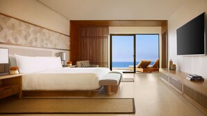 Une chambre d’hôtel moderne dotée d’un grand lit, d’une télévision, d’une vue sur l’océan et d’un balcon avec un fauteuil de relaxation.