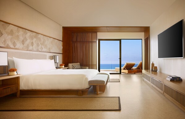 Habitación de hotel moderna con una cama grande, televisión, vista al océano y balcón con una silla de descanso.