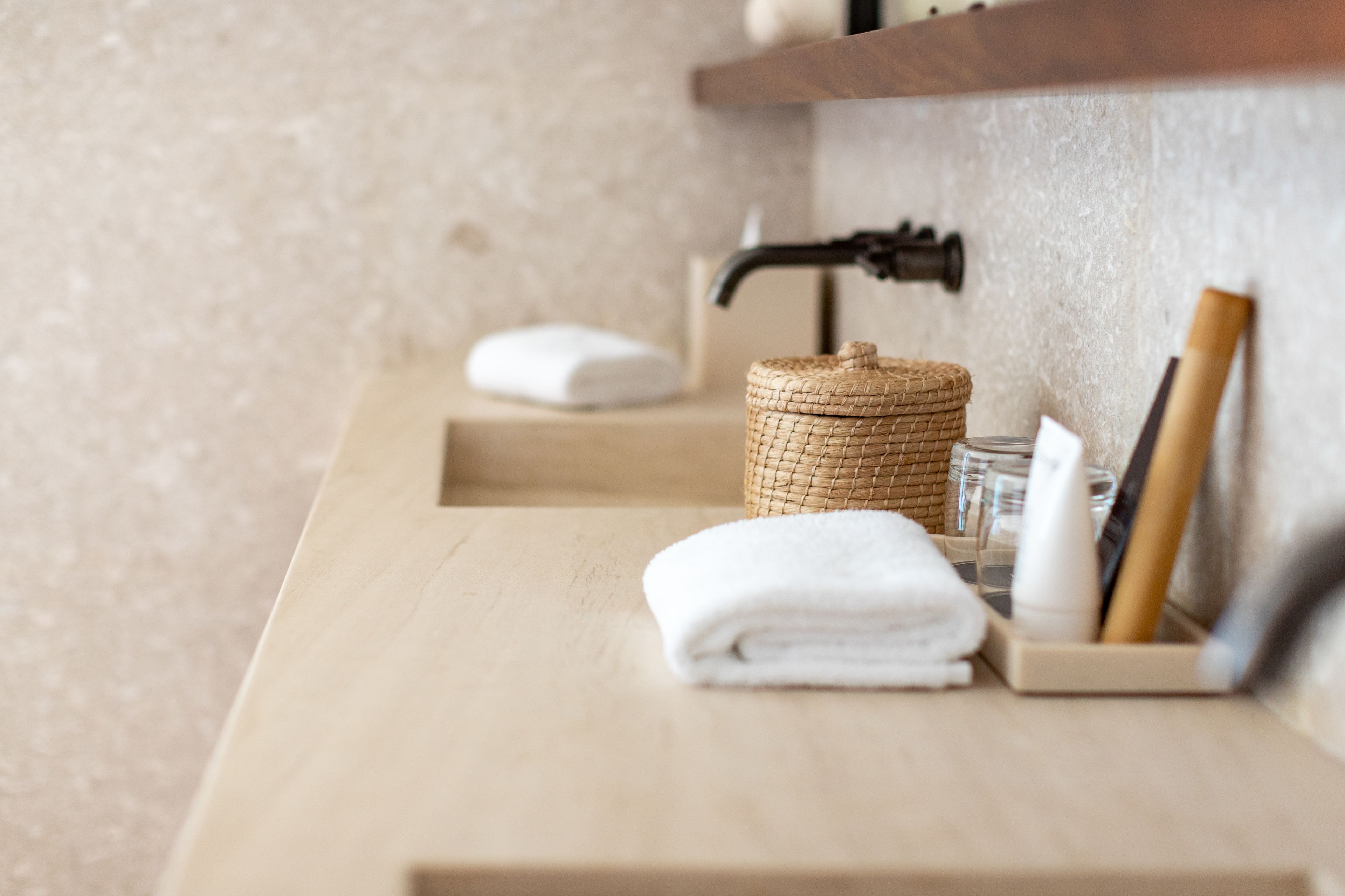 A bathroom with a wooden countertop, a woven basket, a folded towel, a soap dispenser, and a razor.