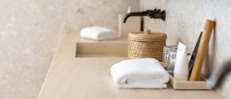 A bathroom with a wooden countertop, a woven basket, a folded towel, a soap dispenser, and a razor.