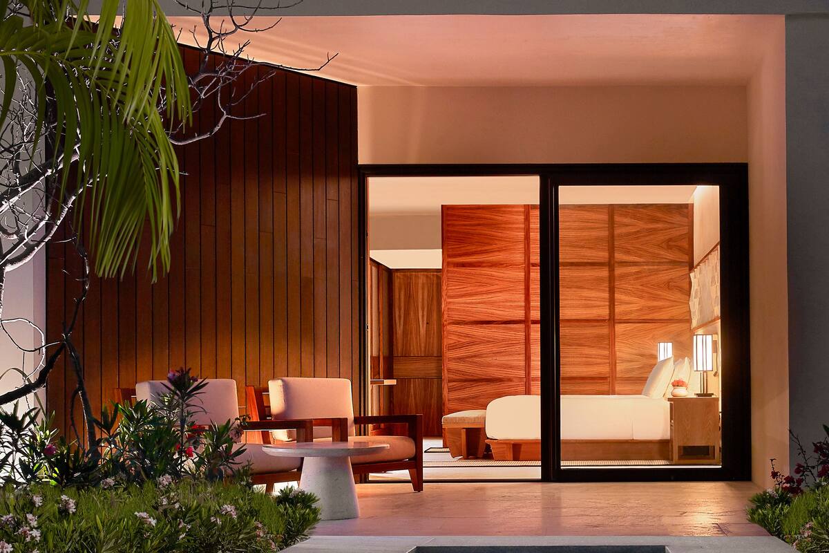 A modern hotel room with a large sliding glass door, a pool, and a seating area with a table and chairs.