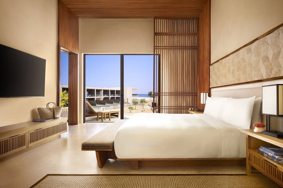 A modern hotel room with a large bed, a television, a seating area with a view of the beach, and a large window.