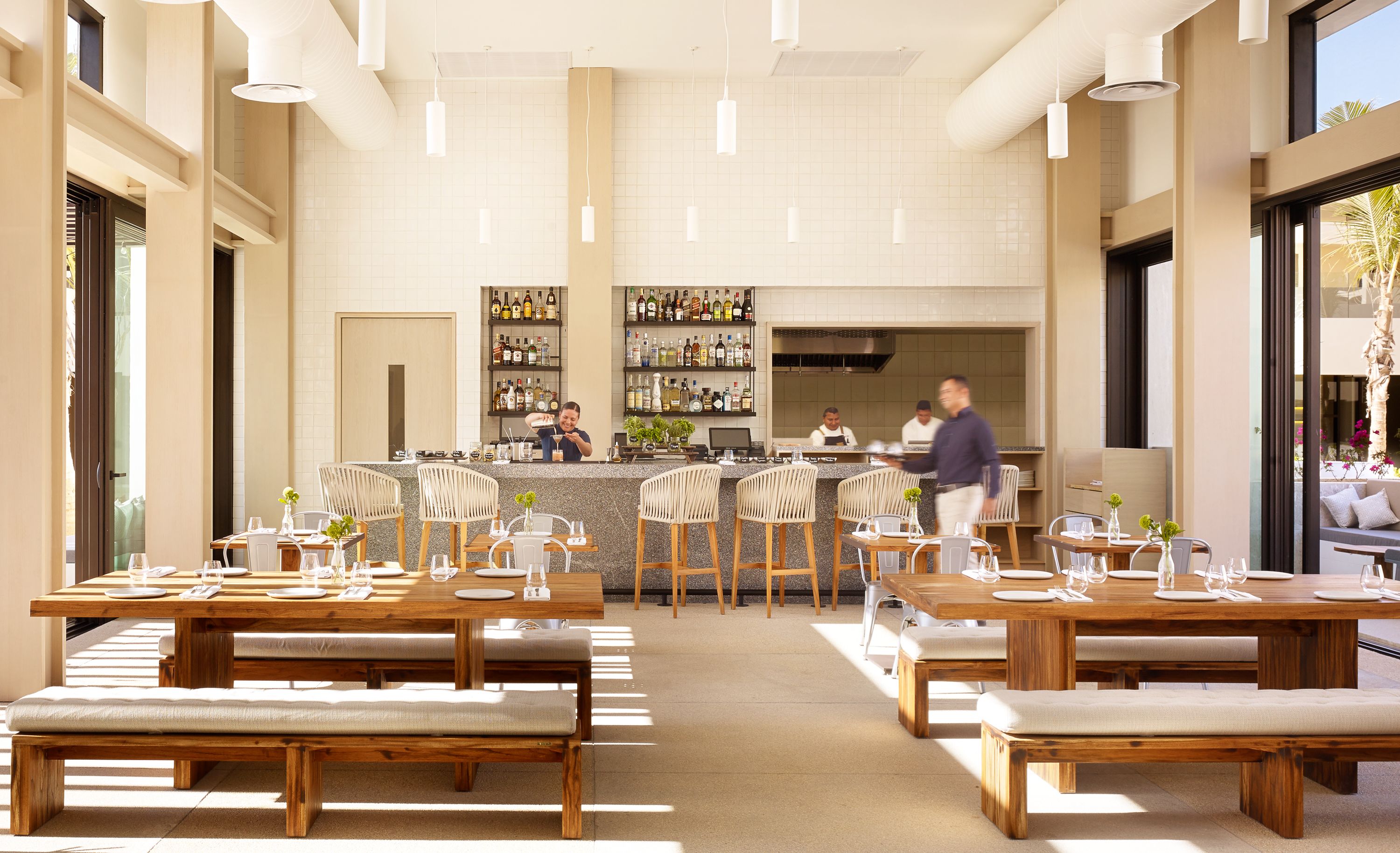 Een restaurant met houten tafels en banken, een bar met flessen op de planken, en uitzicht op het omliggende landschap.