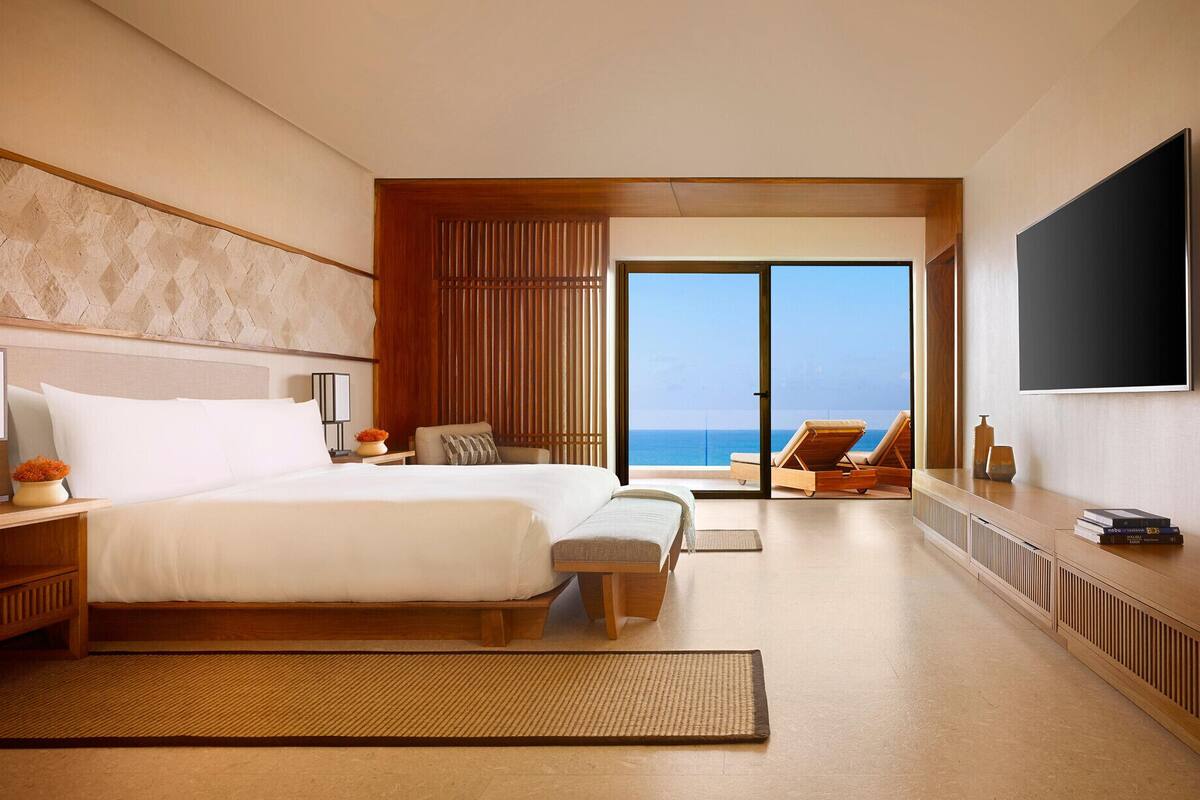 A hotel room with a large bed, a sofa, a TV, and a view of the ocean.