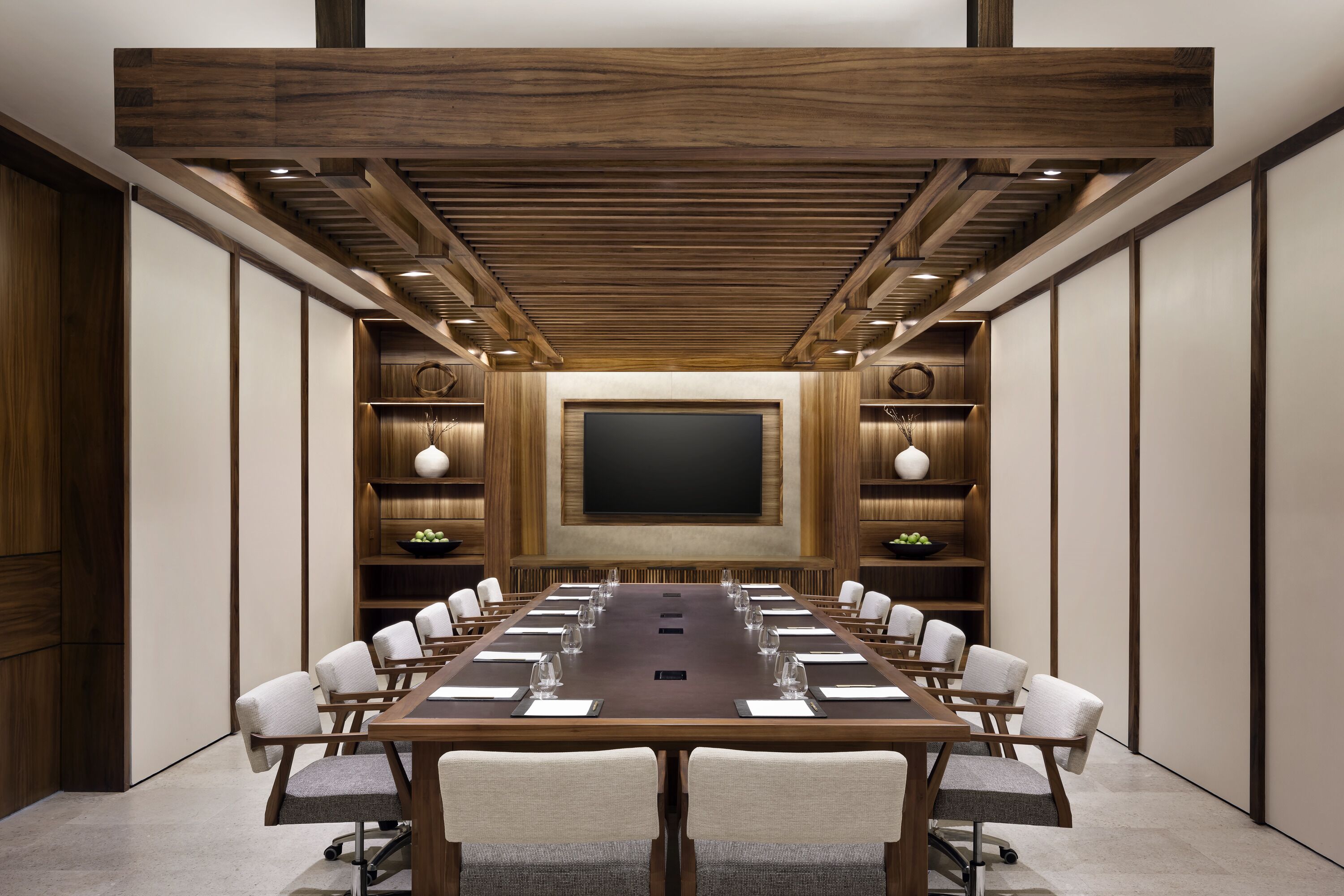 Un salón de conferencias con una larga mesa, sillas, una pantalla grande y paneles de madera.