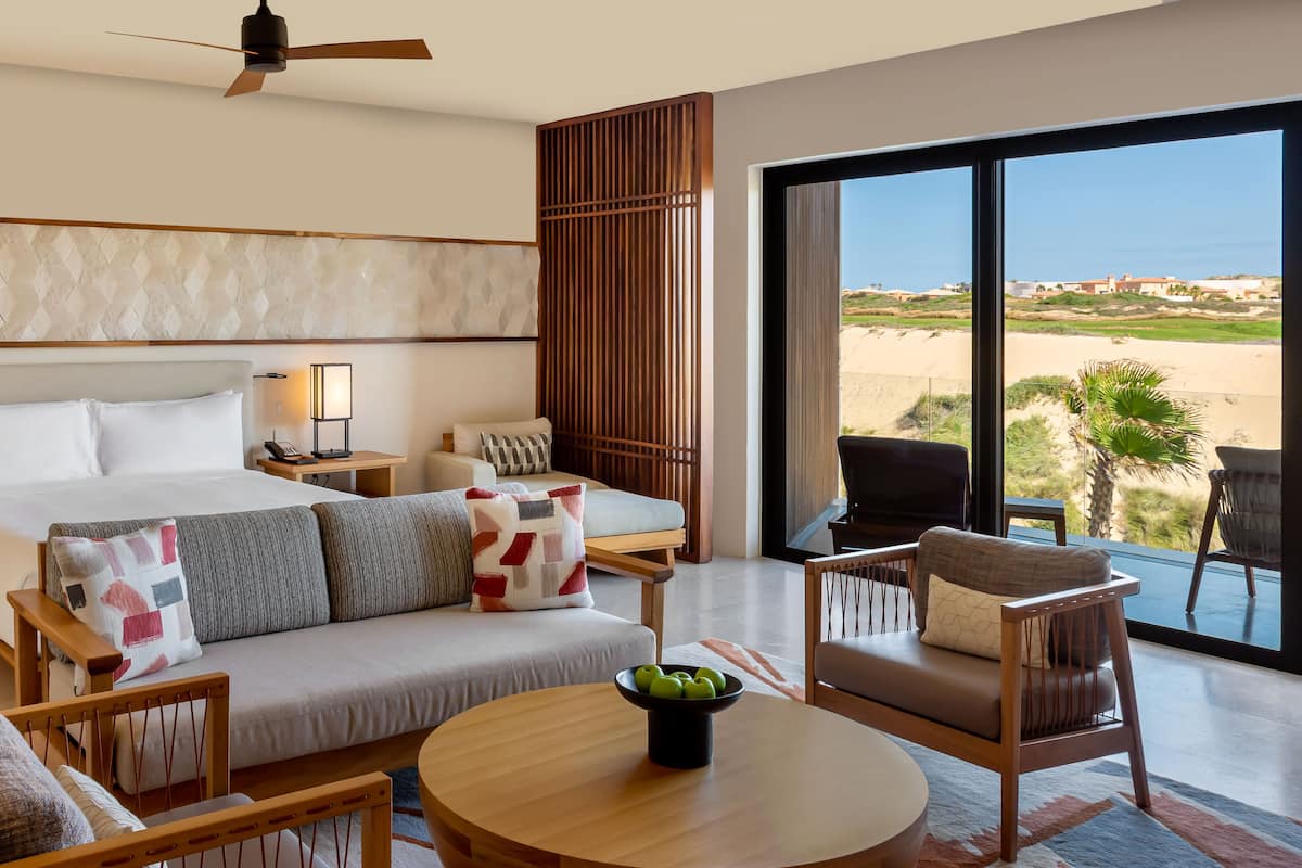 A hotel room with a large bed, a sofa, a dining table, and a view of the beach.
