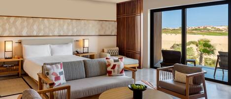 A hotel room with a large bed, a sofa, a dining table, and a view of the beach.