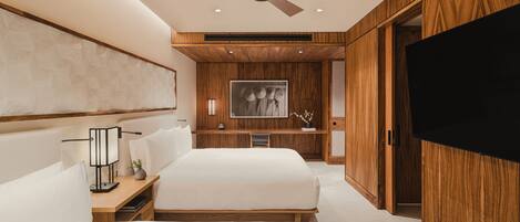 A modern bedroom with a large bed, wooden paneling, a ceiling fan, a flat-screen TV, and a desk with a lamp.