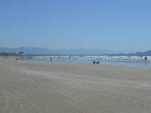 A wide sandy beach with a few umbrellas and people scattered along the shore.