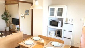 A dining area with a wooden table set for two, a microwave, and a refrigerator in the background. - Villa Sans Company (Ishigaki)
