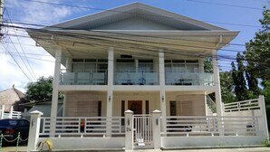 A two-story building with a balcony on the upper floor, a gated entrance, and a thatched-roof structure in the background.