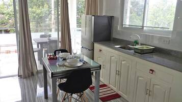 A compact kitchen with a dining area, a refrigerator, a sink, and a window with blinds.