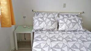 A bedroom with a bed featuring a geometric patterned bedspread, a bedside table with a lamp, and a small nightstand.