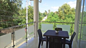 A balcony with a table and chairs, a potted plant, and a view of a road and greenery.