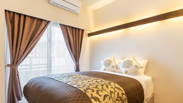 Habitación de hotel con una cama grande, cortinas, una mesita de noche y un aire acondicionado instalado en la pared.