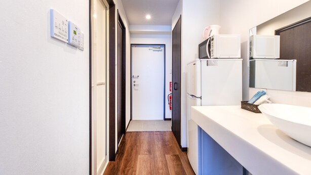 A narrow hallway with a wooden floor, a white sink, and a microwave on a counter.
