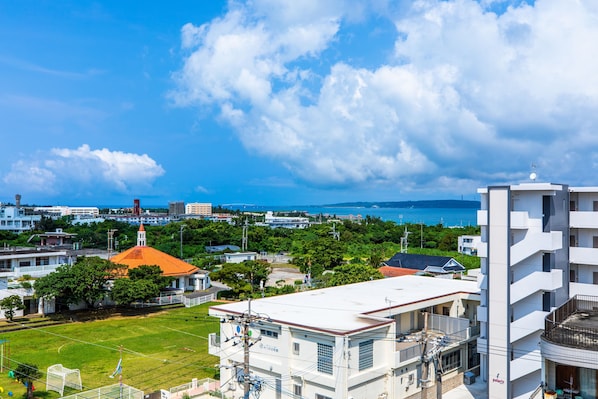 A residential area with a large white building, a red-roofed structure, and a view of the sea.