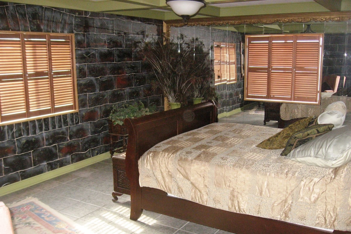 Un dormitorio con una cama grande, una mesita de noche, una planta en maceta y un espejo.