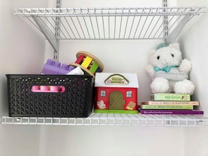 Una estantería con una casa de juguete, un peluche y libros infantiles.
