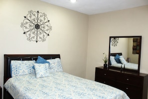 Un dormitorio con cama, cómoda, espejo y un adorno en la pared.