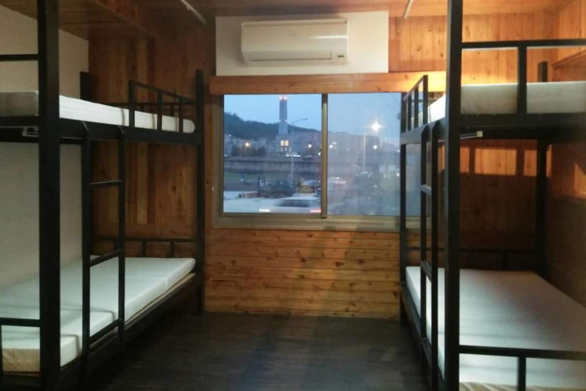 A bunk room with wooden walls and a window overlooking a cityscape.
