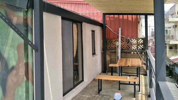 Un balcón con una mesa y sillas de madera, un edificio blanco con techo rojo y vistas a edificios vecinos.