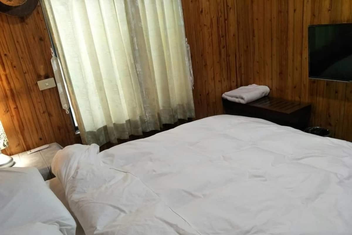 A bedroom with a wooden wall, a bed with white bedding, a nightstand, and a television on the wall.