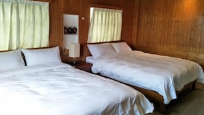 Una habitación con dos camas individuales, paredes de madera, una mesita con botellas y una ventana con cortinas.
