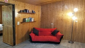 Una habitación con paredes de madera, un sofá rojo, un tapete estampado, un escritorio con lámpara y una puerta con un cartel que dice 'A'.