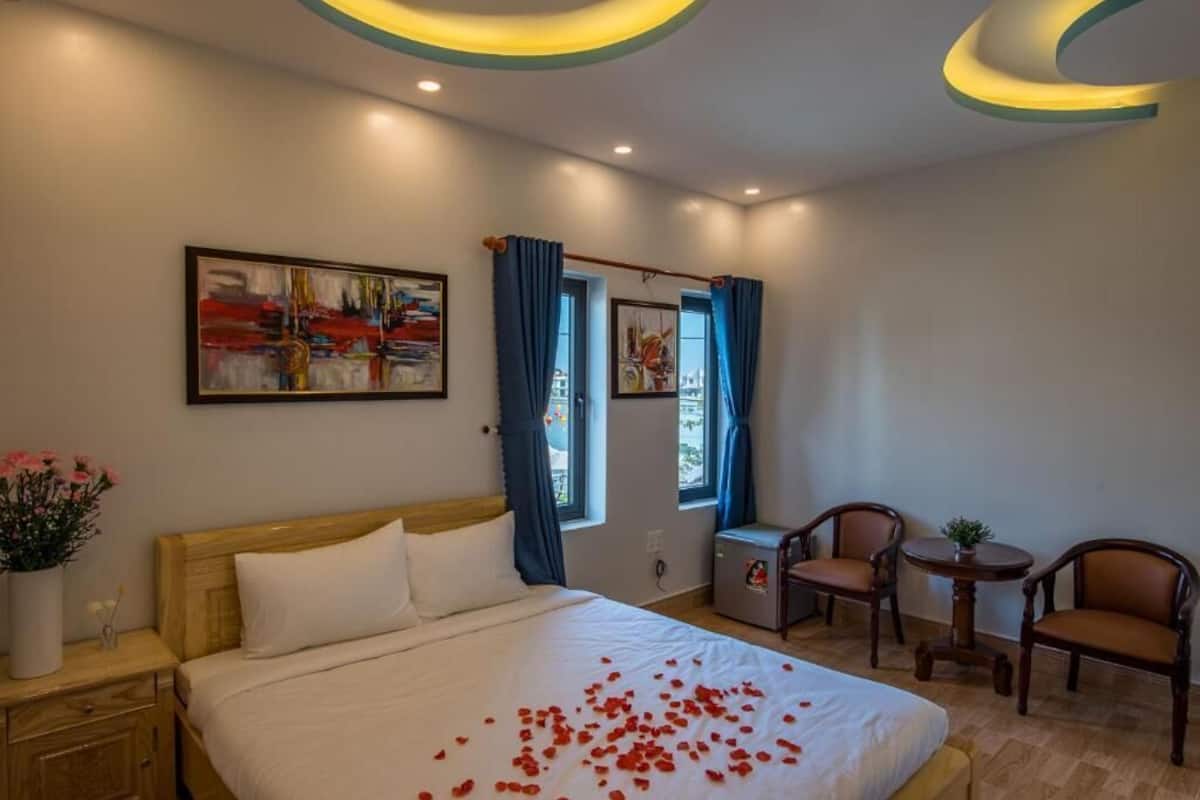 A hotel room with a bed, a desk, two chairs, a small table, and artwork on the walls.