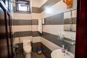 A modern bathroom with a toilet, bidet, and sink, featuring striped tile walls and a glass shower enclosure. - Minh An Riverside Villa (Da Nang)