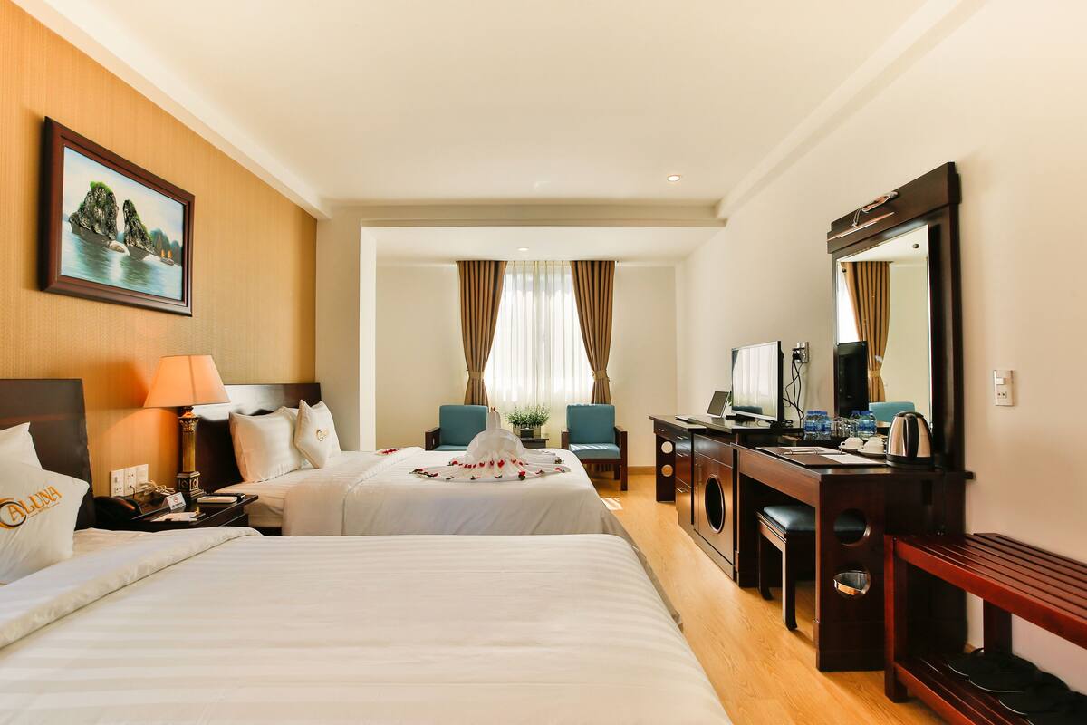 Habitación de hotel con dos camas, un escritorio con computadora, un espejo y una ventana con cortinas.
