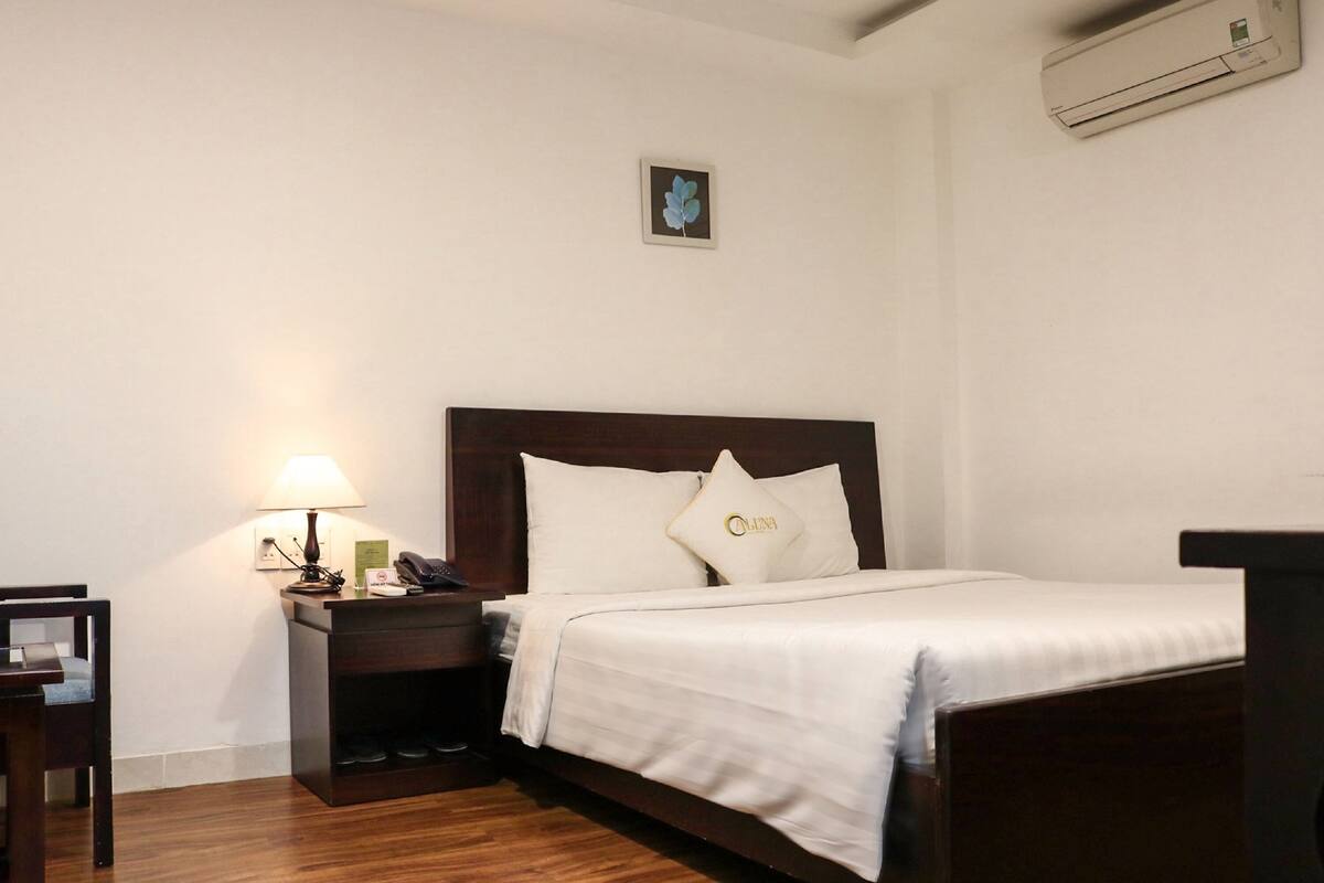 Habitación de hotel con cama, mesita de noche, lámpara, escritorio y aire acondicionado instalado en la pared.