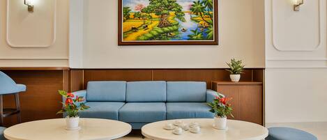 Eine moderne Hotelhalle mit einem blauen Sofa, zwei runden Tischen mit Topfpflanzen und einem gerahmten Gemälde an der Wand.